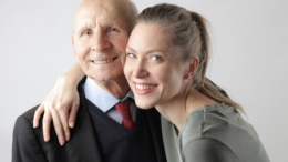 O femeie tânără zâmbește în timp ce strânge în brațe un bărbat vârstniccare are nevoie de îngrijire la domiciliu